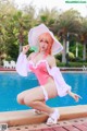 A woman in a pink bathing suit and a white hat by a pool.