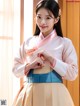 A woman in a pink and blue hanbok is posing for a picture.