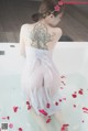 A woman in a white dress sitting in a bathtub with rose petals.