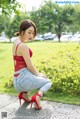 A woman in a red top and jeans crouching down on a sidewalk.