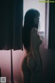 A naked woman standing in front of a window.