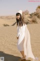 A woman in a white dress and hat standing in the sand.