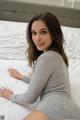 A woman sitting on top of a bed in a gray dress.