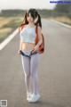 A woman in a white top and blue shorts standing on a road.