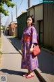 A woman in a purple kimono is standing on the street.