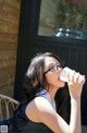 A woman wearing glasses drinking water from a plastic cup.